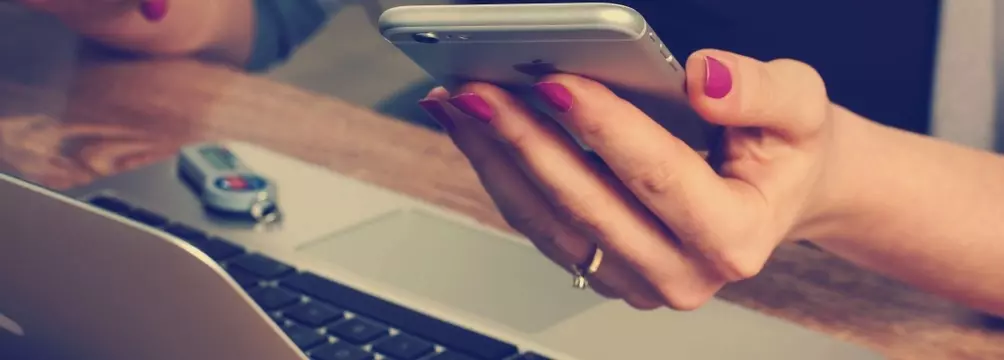 Woman working at laptop with cellphone in hand
